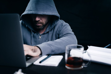 a young hacker is thoughtfully working behind a laptop with a mug of tea