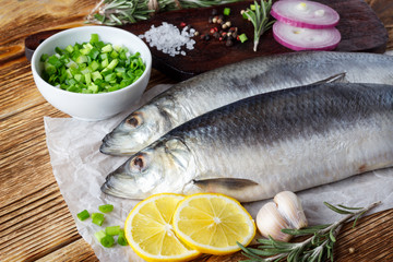 Fish herring with red onion, lemon and spices on the wooden table.
