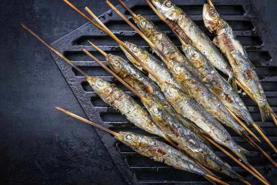 Traditional Spanish barbecue sardines on a wooden skewer as top view on a grillage