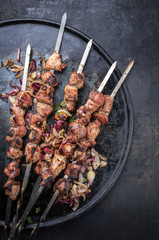 Traditional Russian shashlik on a barbecue skewer with roasted onion as top view on old board with copy space right