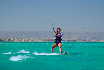 Kite surfing girl in sexy swimsuit with kite in sky on board in blue sea riding waves with water splash. Recreational activity, water sports, action, hobby and fun in summer time. Kiteboarding sport © yanamavlyutova