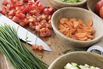 Chopped tomatoes, carrots, and chives on cutting board with knife surrounded by other ingredients.