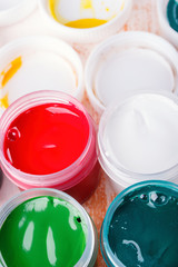 Plastic cans of multi-colored gouache on a wooden painted table