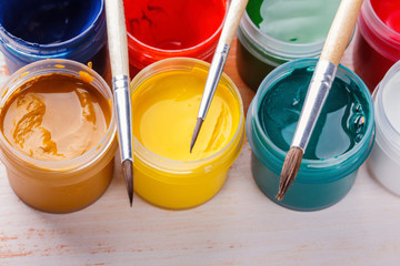 brush on the Plastic cans of multi-colored gouache on a wooden painted table