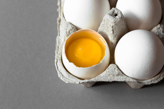 Close Up Broken Egg Yolk In Carton On Gray Background. Horizontal Photo