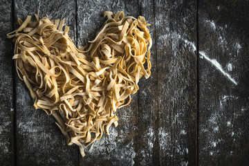 Prepared Italian traditional tagliatelle in heart shape on wooden background with blank...