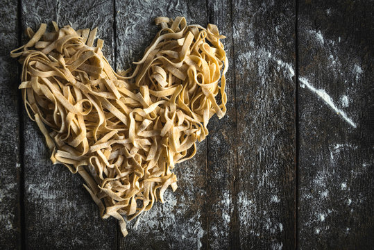 Prepared Italian traditional tagliatelle in heart shape on wooden background with blank space,Valentine day concept