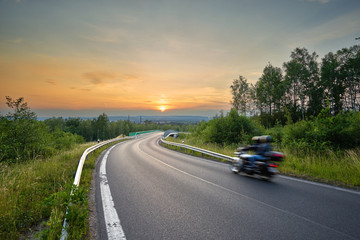 Motion-blurred motorcycle on the road in a forest overlooking the countryside at sunset