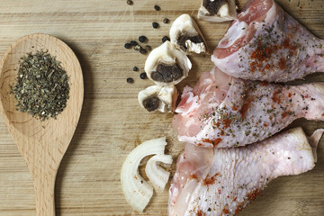 Fresh, raw, uncooked chicken drumsticks with onion, mushrooms and spices on a wooden cutting board