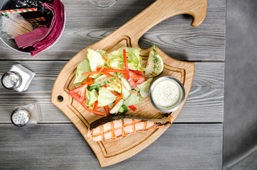 Top view Grilled salmon steak with tartar sauce and fresh vegetables served on a wooden table at restaurant. Grey background with space for text. Pepper and salt, Knife and fork, metal