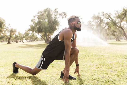 Black man crouching in park stretching legs