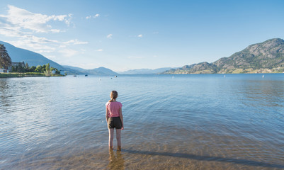 Young girl standing in Skaha Lake with back to camera looking north toward Penticton