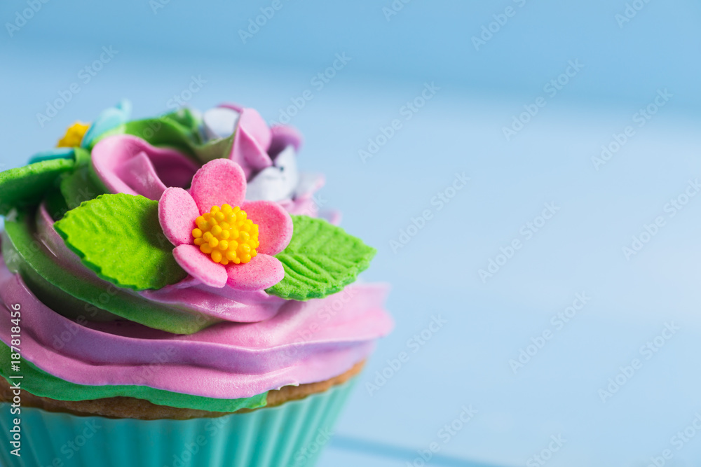 Wall mural closeup cupcake creamy multicolored top decorated with colorful flowers and leaves on blue backgroun