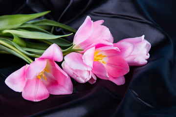 Beautiful bouquet of tender pink tulips lying on black satin fabric