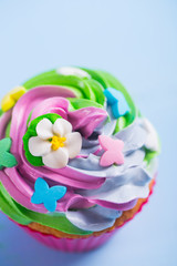 Fototapeta na wymiar Closeup cupcake creamy multicolored top with colorful flowers and butterflies on blue background