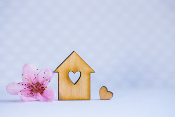 Obraz na płótnie Canvas Wooden house with hole in form of heart and pink cherry flower on blue background