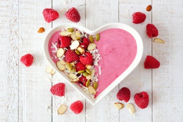 Healthy raspberry smoothie in a heart shaped bowl with superfoods. Above scene on a white wood...