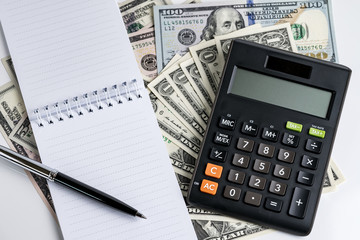 Notepad and pen, calculator on pile of dollar banknotes using as business accounting or tax calculation concept