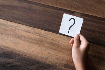 hand holding a note written a question mark on a wooden table background