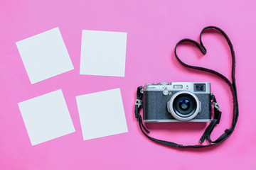 Vintage photo camera on Valentine's Day pink background with composition of blank photo frames, empty notes and hearts, top view. flat lay
