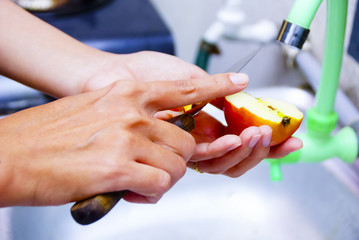 Female Hands Cutting And Peeling Skin Off Of Red Apple Using Sharp Knife At Kitchen Sink