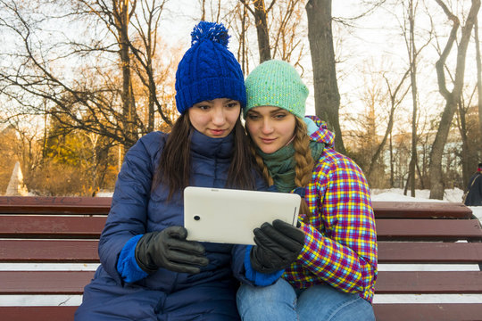 Caucasian women sitting on park bench in the winter holding digital tablet