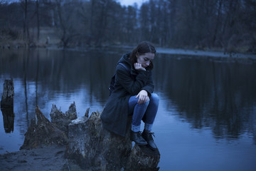 Caucasian woman sitting on tree stump near river thinking