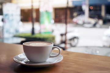 Closeup image of a white cup of latte coffee on wooden table in cafe with blur background