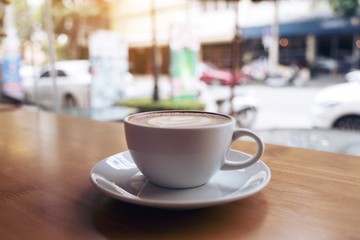 Obraz premium Closeup image of a white cup of latte coffee on wooden table in cafe with blur background