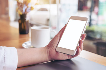 Mockup image of a woman's hand holding white mobile phone with blank desktop screen and coffee cup in cafe