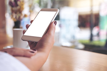 Mockup image of a woman's hand holding white mobile phone with blank desktop screen and coffee cup in cafe