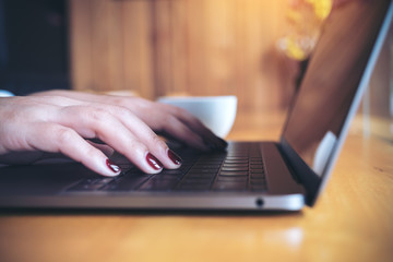Closeup image of a business woman's hands working and typing on laptop keyboard on wooden table