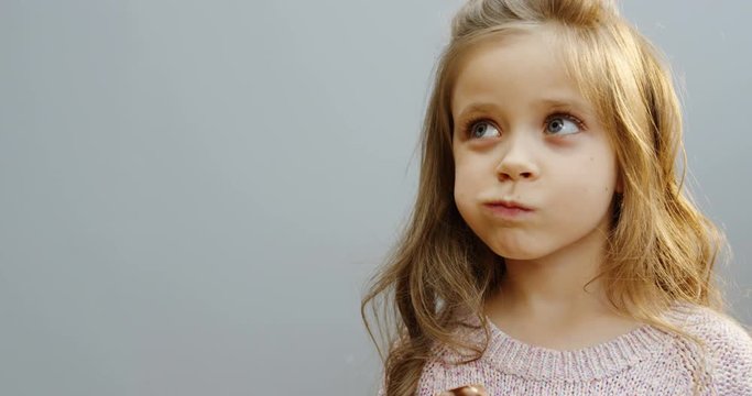 Close up of the blonde lovely funny little girl biting and eating a chocolate bar in front of the camera. White wall background. Portrait. Indoors