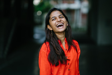 Portrait of attractive and young Indian woman laughing in an orange ethnic dress during the day
