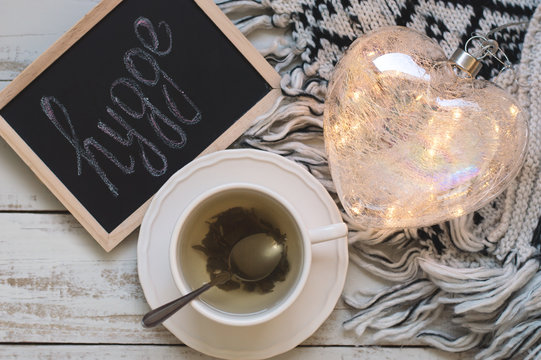 Cup of green tea, heart shaped lantern for house decoration, knitted blanket and blackboard with text "hygge". Hyggelig. Hygge concept. Top view