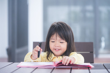 Cute little girl doing homework, reading a book, coloring pages, writing and painting. Children paint. Kids draw. Preschooler with books at home. Preschoolers learn to write and read. Creative toddler