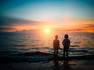 Little boy and girl stand together on the beach and looking at sea, while sunset, Holiday concept