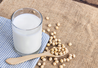 Soy milk in a glass with soybeans in spoon on sackcloth background.