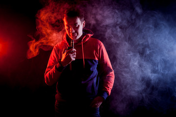 Man in sport hoody vaping an electronic cigarette.Isolated on black background.Around  clouds of smoke