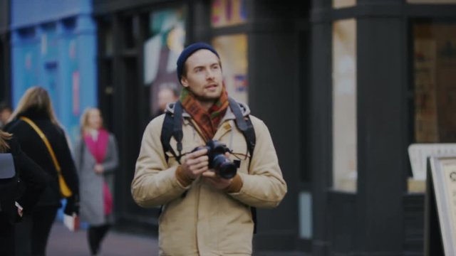 Young male photographer taking photos as he walks through a crowd on the high street, in slow motion