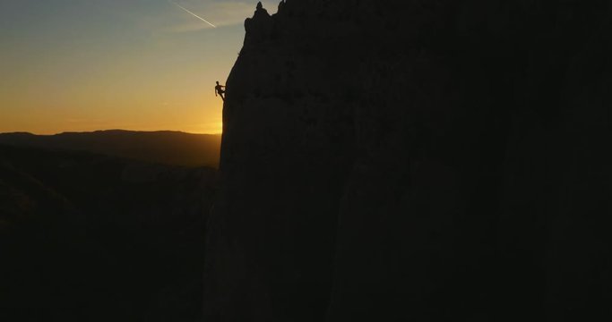 Aerial wide shot of a rock climber descending the wall  at amazing evening sunset light.
