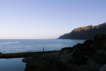 Man standing near natural pool next to ocean at dawn