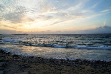 Obraz premium Beautiful sunset scenic wavy seaview and natural rock beach with beautiful shades of soft orange and blue sky and abstract cloud background