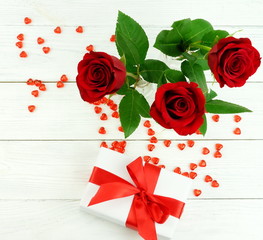 Valentine's day. Bouquet of beautiful red roses in a vase, gift and red hearts on a white wooden background. flat lay. top view. copy space