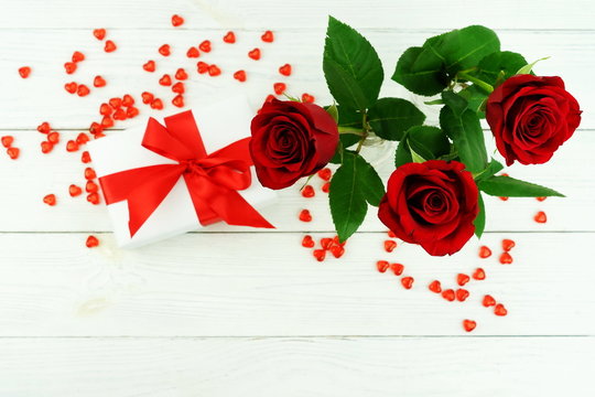Valentine's day. Bouquet of beautiful red roses in a vase, gift and red hearts on a white wooden background. flat lay. top view. copy space