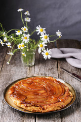 Traditional homemade banana caramel pie on vintage wooden table decorated a bouquet of chamomiles. Upside down banana cake. Selective focus 