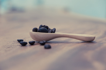Coffee beans in a wooden spoon on a table. (vintage tone)