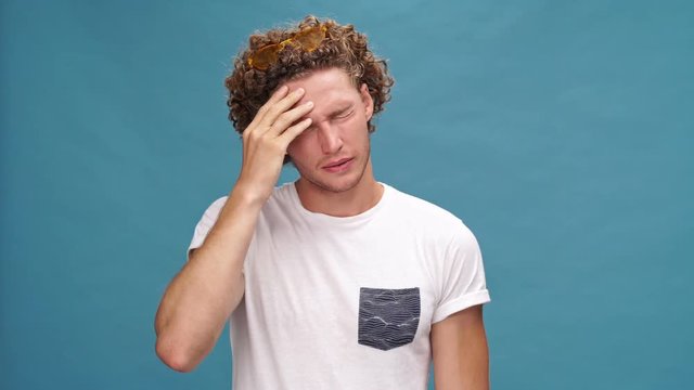 Confused curly man in t-shirt forgot something to do over blue background