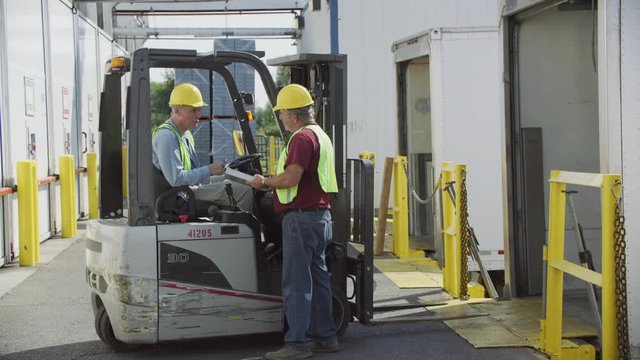 Truck driver and forklift driver talk at shipping facility