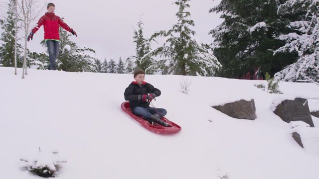 Young boy sledding down snow covered hill in winter